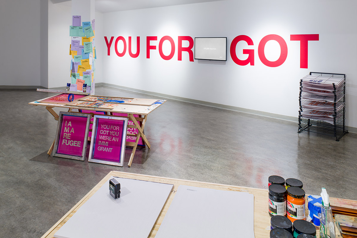 tables set for screenprint workshop in the foreground, tv monitor and large red letters 