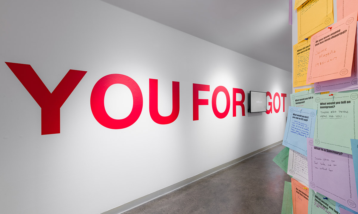 Image of colorful questionnaire papers attached to a while column wall, large red letters on a white wall the the background