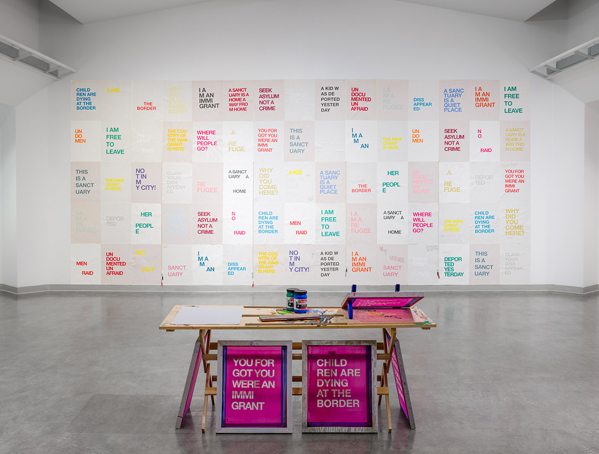 table set up for screenprinting workshop in front of a large wall covered with a grid of printed posters.