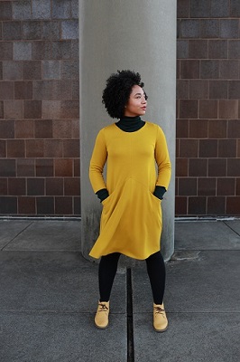 Aerica standing in front of a concrete pillar and brick wall. 