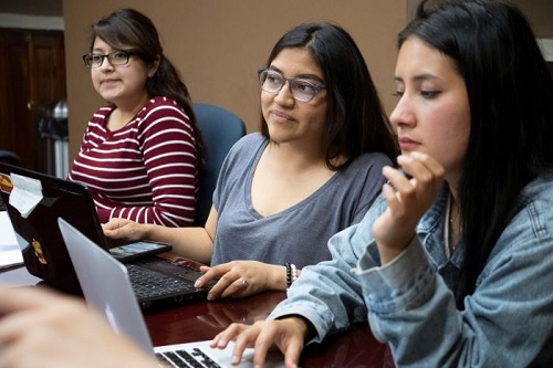 Three students doing research on a laptop computer.