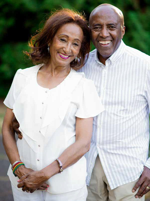 Ezra and his wife Yobi standing in front of greenery.