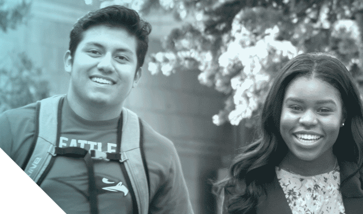 Two students smiling, standing in front of a brick building.