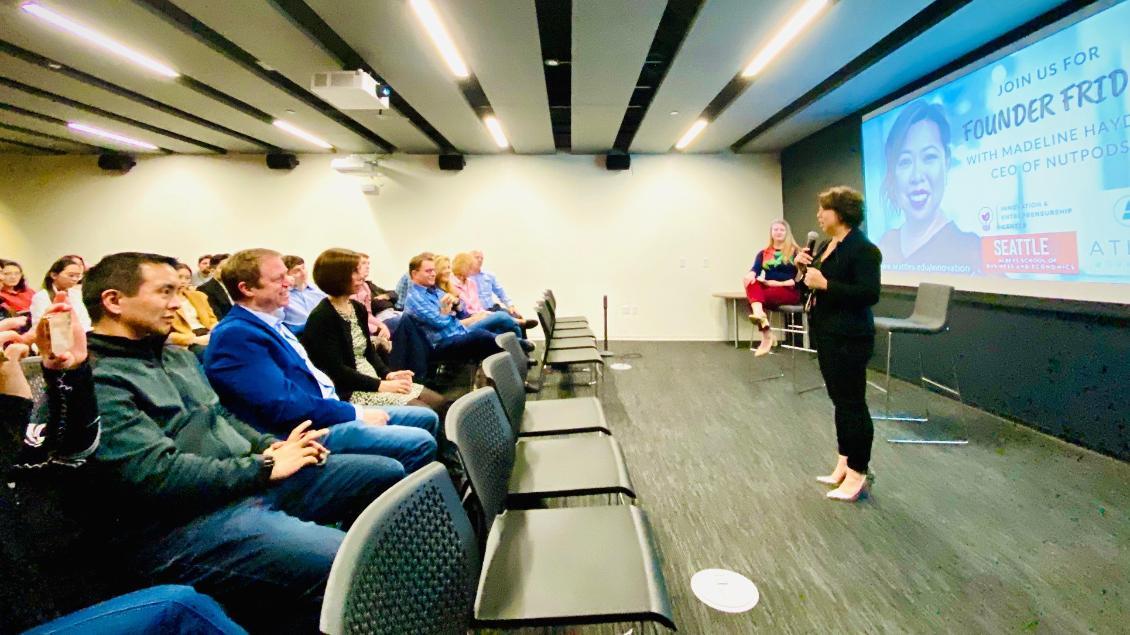 A group of seated audience watching a speaker in front of the room