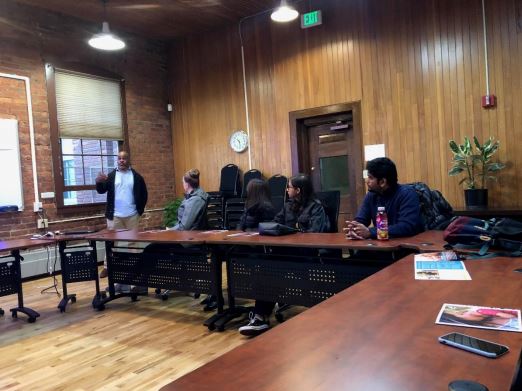 People sitting at a table watching a speaker