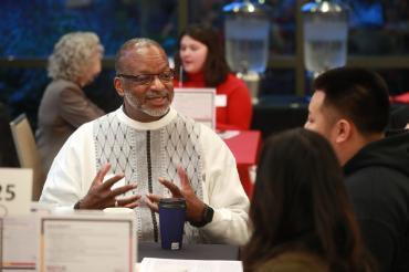 An African American male speaking to a group of people on a round table