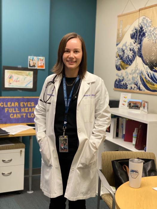 Naomi Diggs profile picture wearing her doctor's coat in her office with a bookshelf in the background