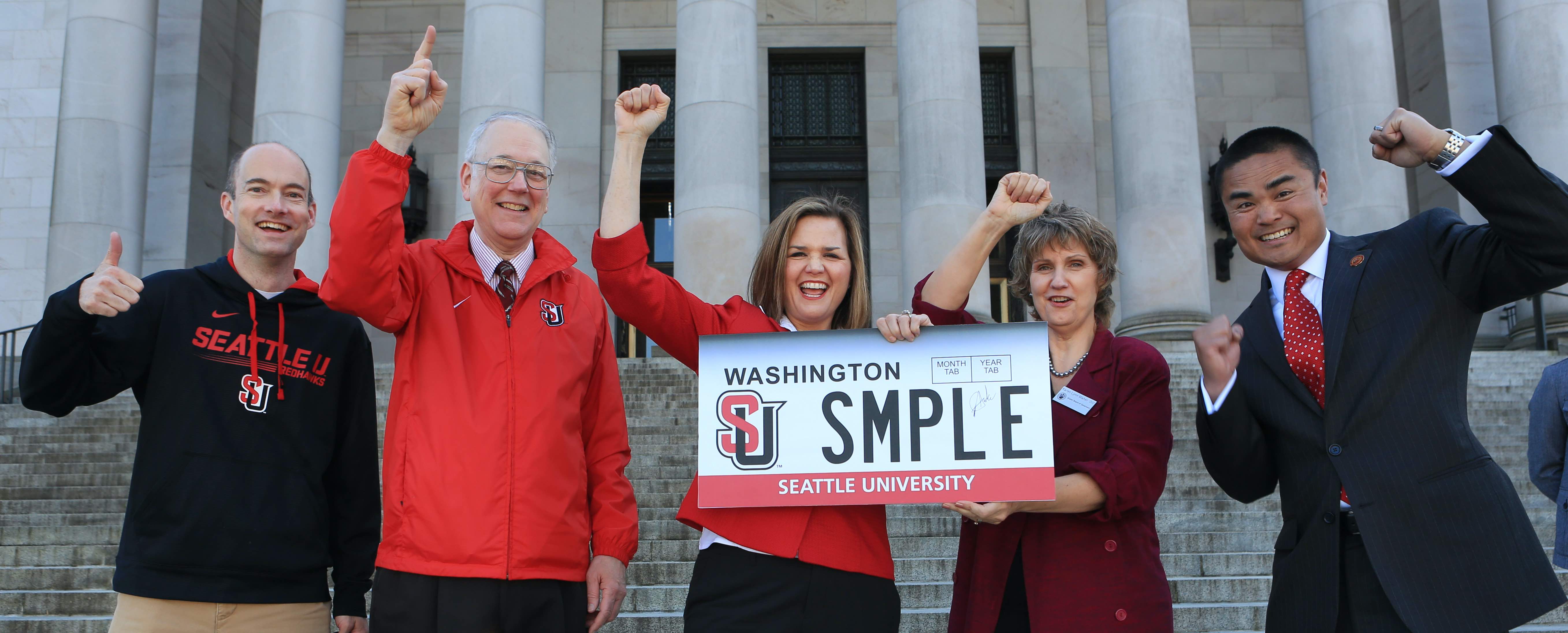 Alumni gather on building steps with a huge SU branded license plate