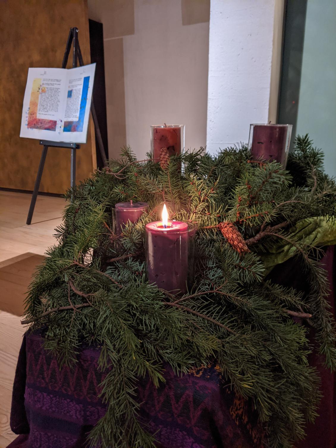 The altar area of Chapel of St Ignatius An advent wreath with four candles and only one candle lit with an image of illuminated Gospel books in the background