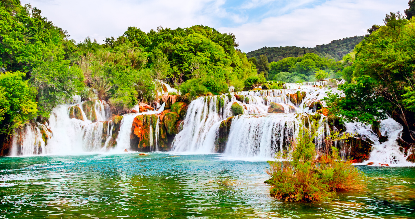 waterfall into a pool of water with trees and sky in background