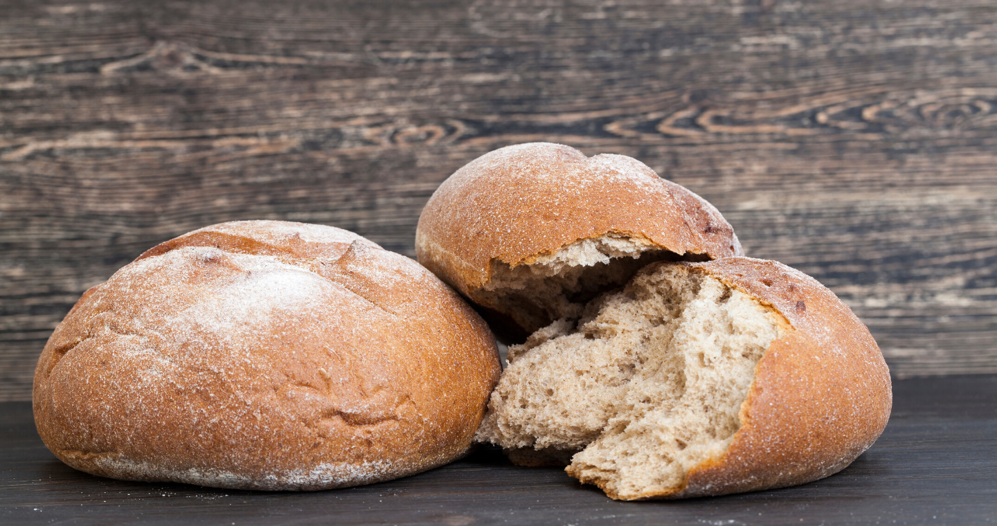 two loaves of bread, one broken, one whole, against a wood background. 