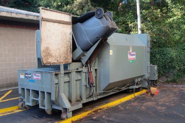 A trash can being dumped into a compost compactor.