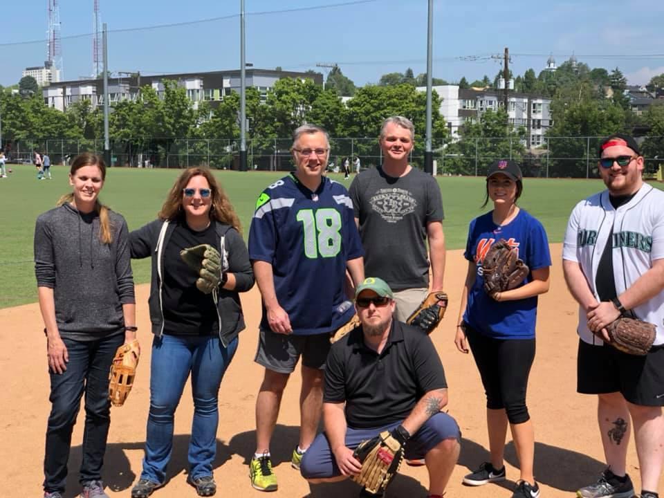 A group of people with baseball mitts at a baseball field on a sunny day