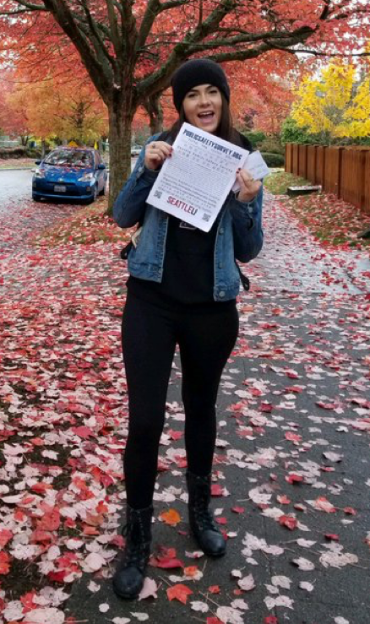 Person holding flyer standing outside on sidewalk with trees