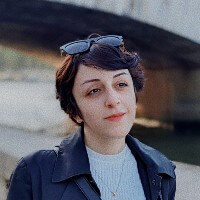 Yasmine Ansari near a river with a bridge in the background