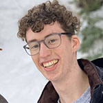 headshot of a smiling person with brown curly hair wearing glasses 