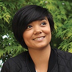 Woman sitting in front of leafy shrub.