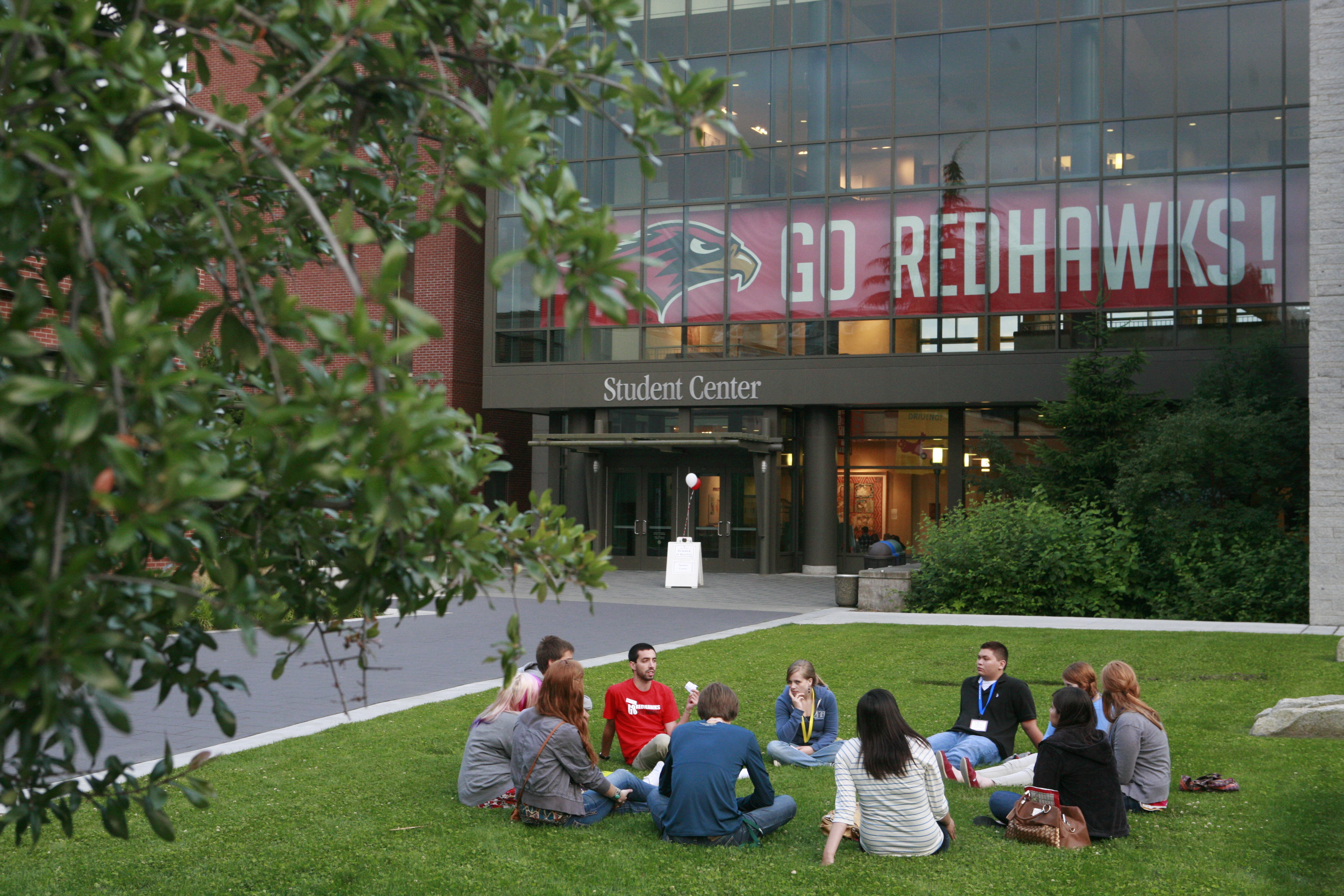 Students sitting in a circle on grass in front of SU student center