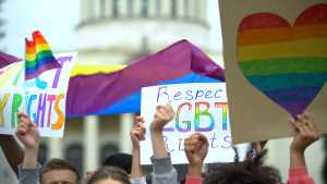 LGBTQ+ supporters hold signs in front of capitol.