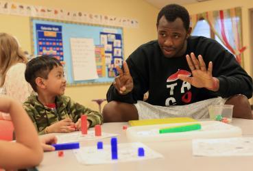 Student teaching a young child in a classroom