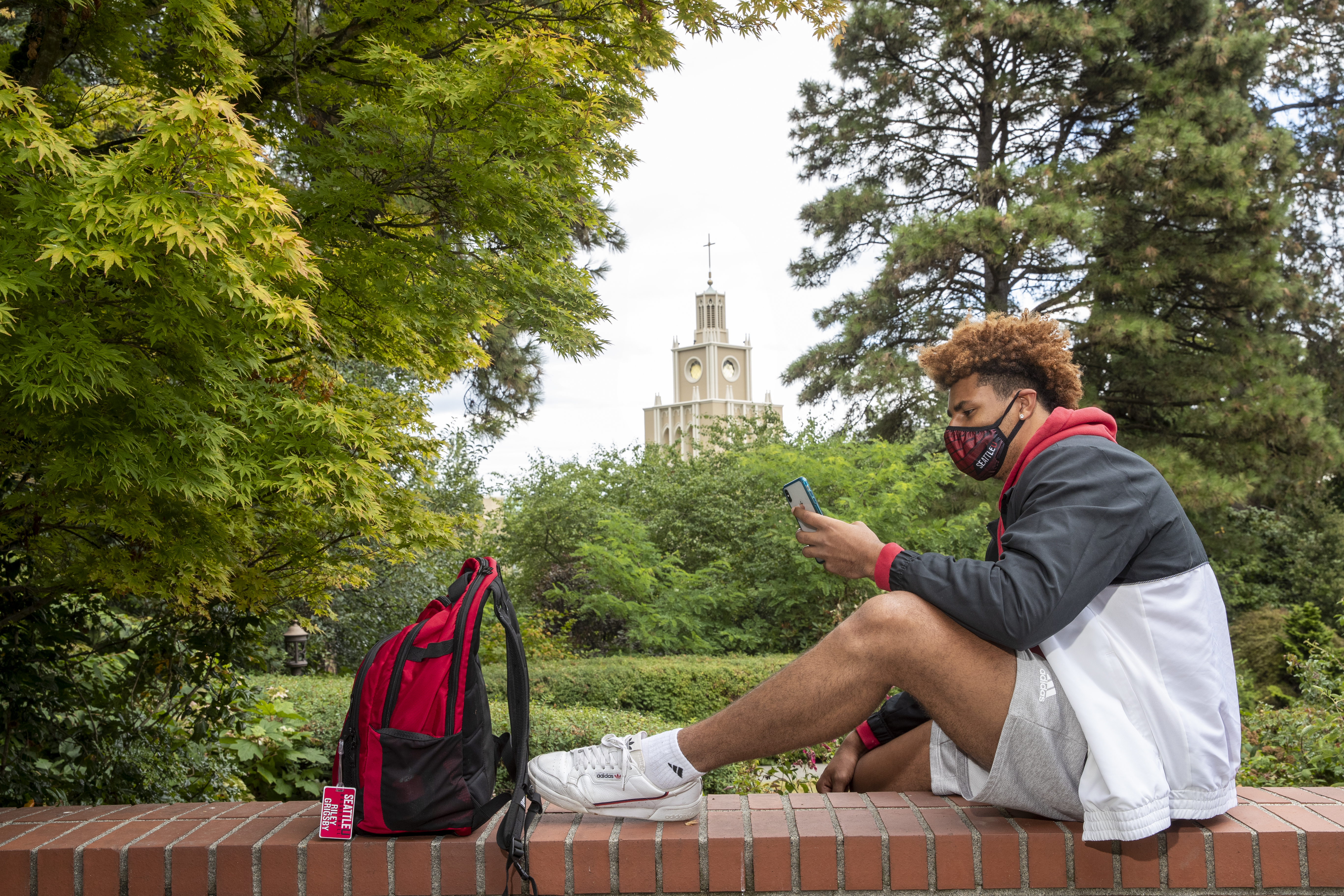 Student sitting on a brick wall wearing an SU mask