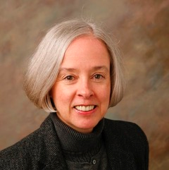 Woman headshot, dark sweater, tan background