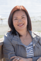 Lynette Pang smiling, sun shining on her, on a bench at a beach