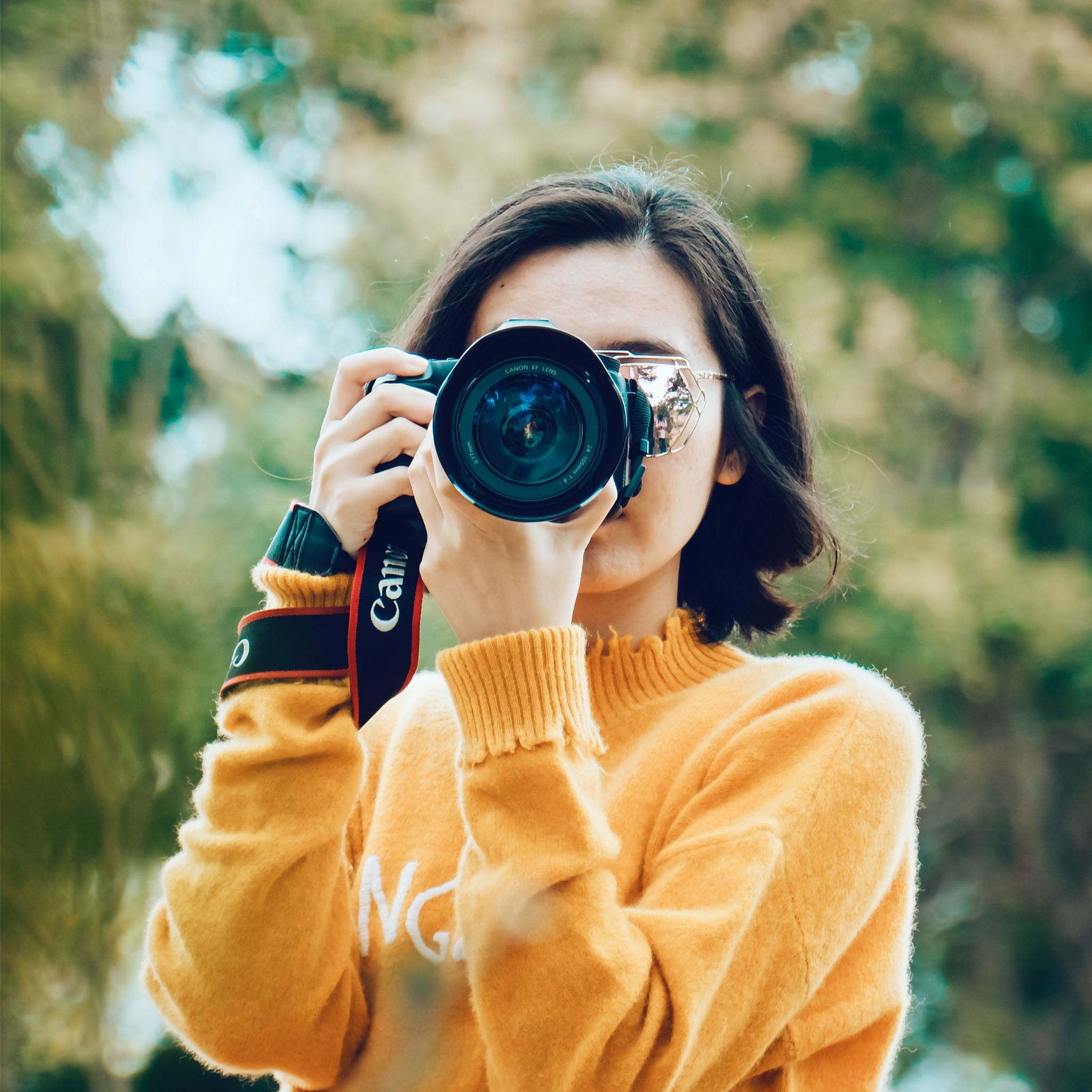 Person taking a photo using a camera with the lens pointed at viewer