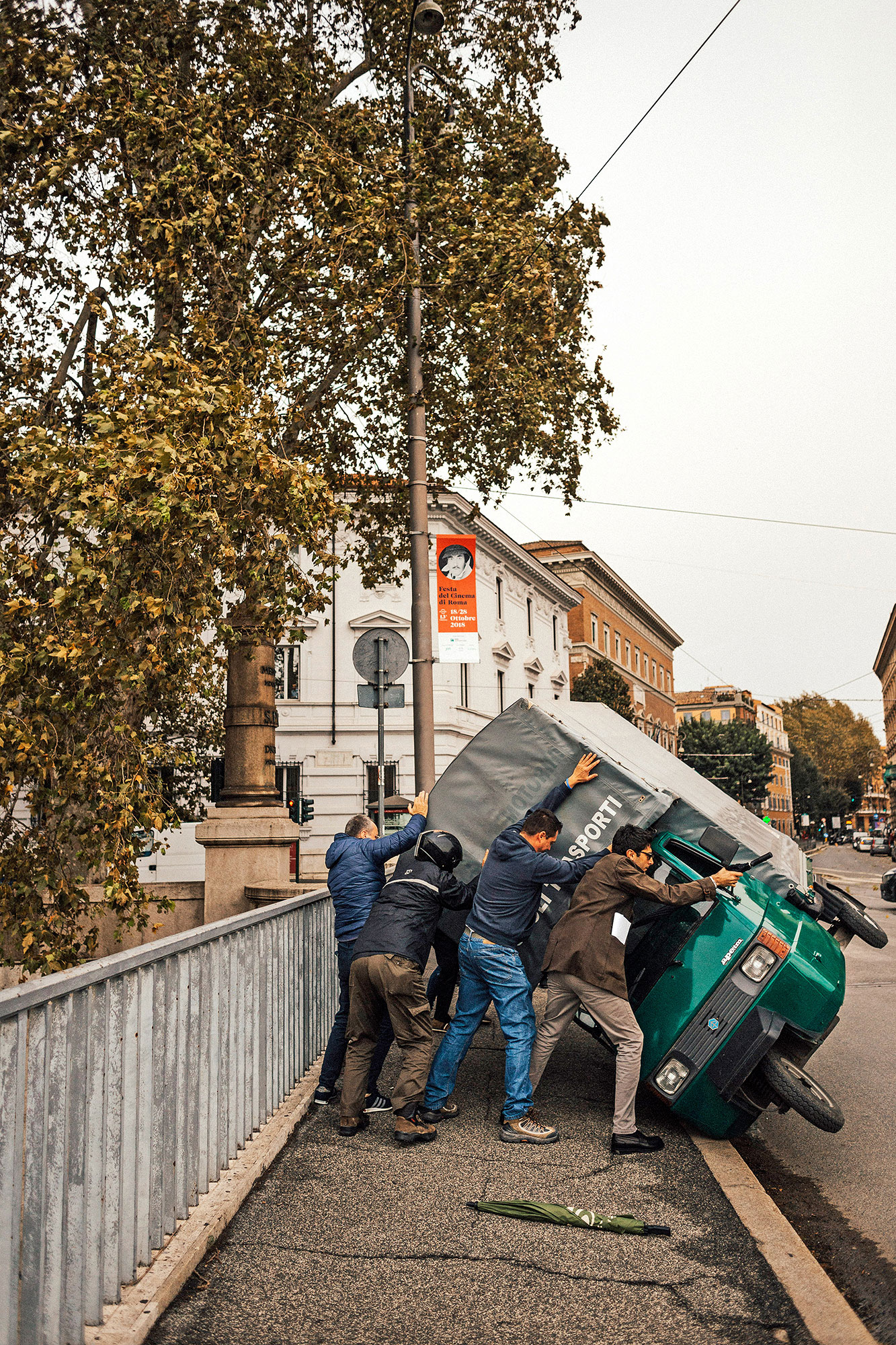 a group of four help right a dark green scooter that has tipped over the sidewalk