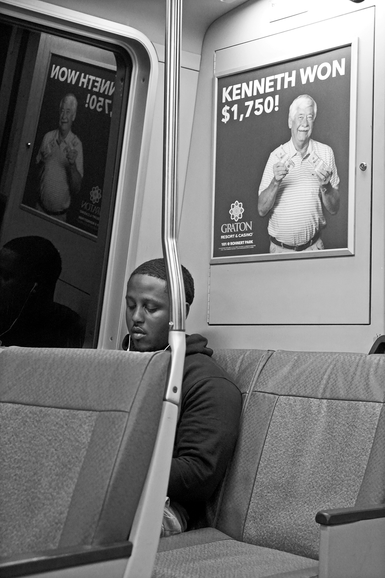 young man riding in transit car with a casino ad in the background