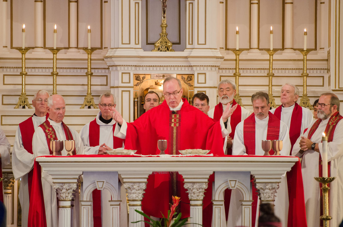 President Sundborg stands at a podium with several SU Jesuits behind him