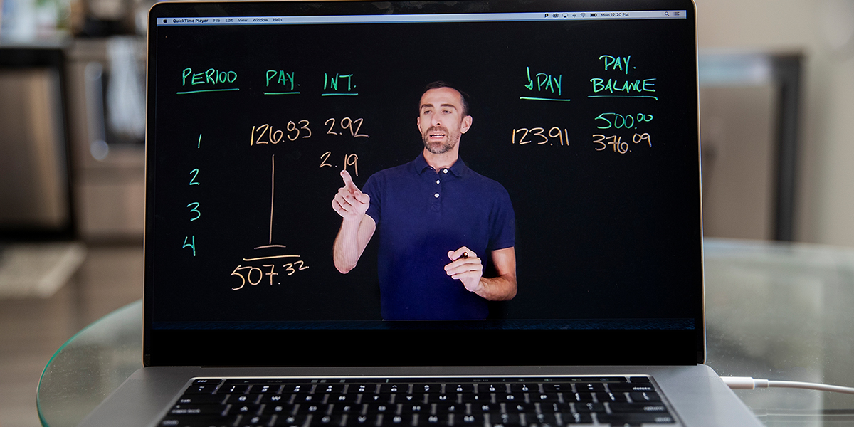 Laptop screen shows instructor facing camera and writing on specialized transparent whiteboard.