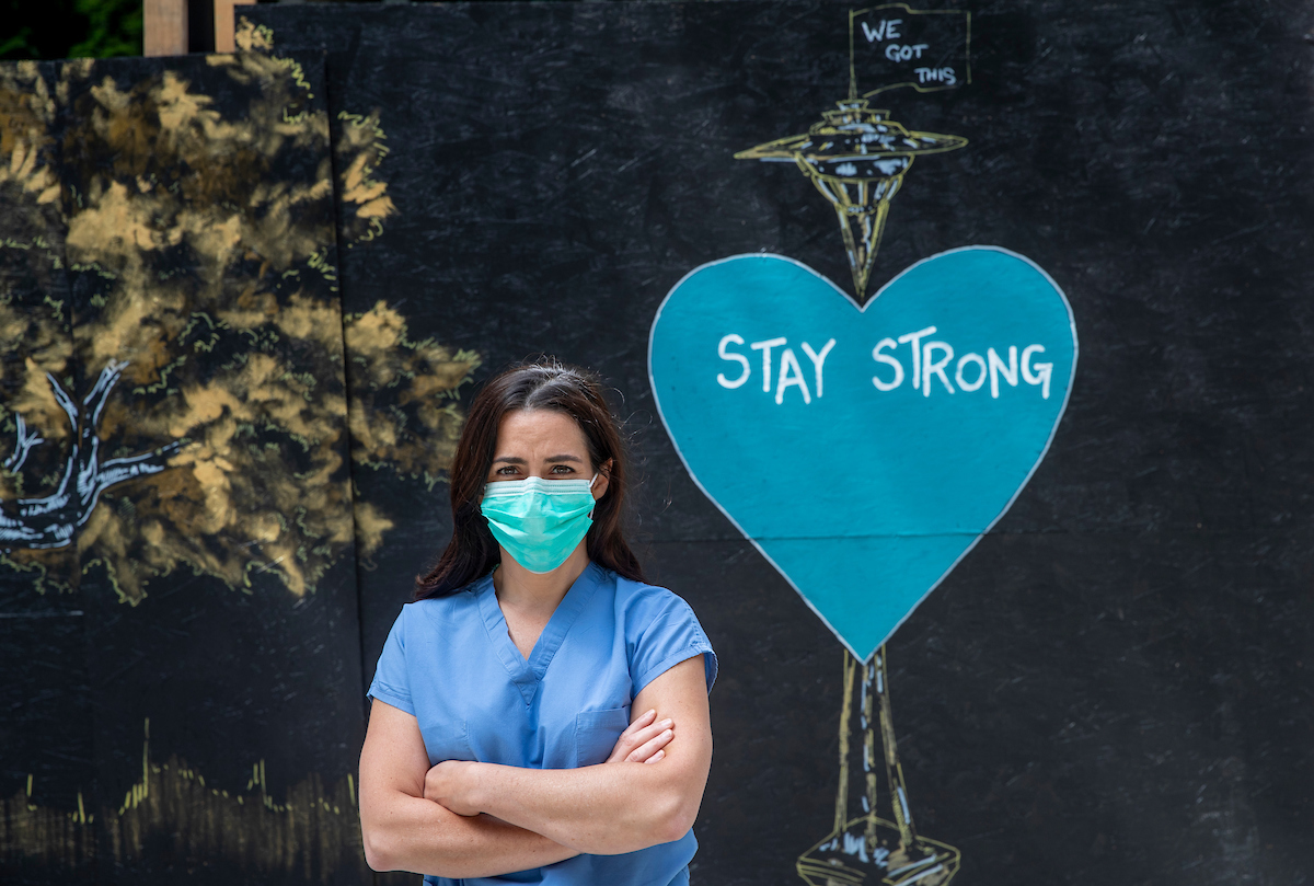 Female nurse wearing face mask stands with arms crossed.