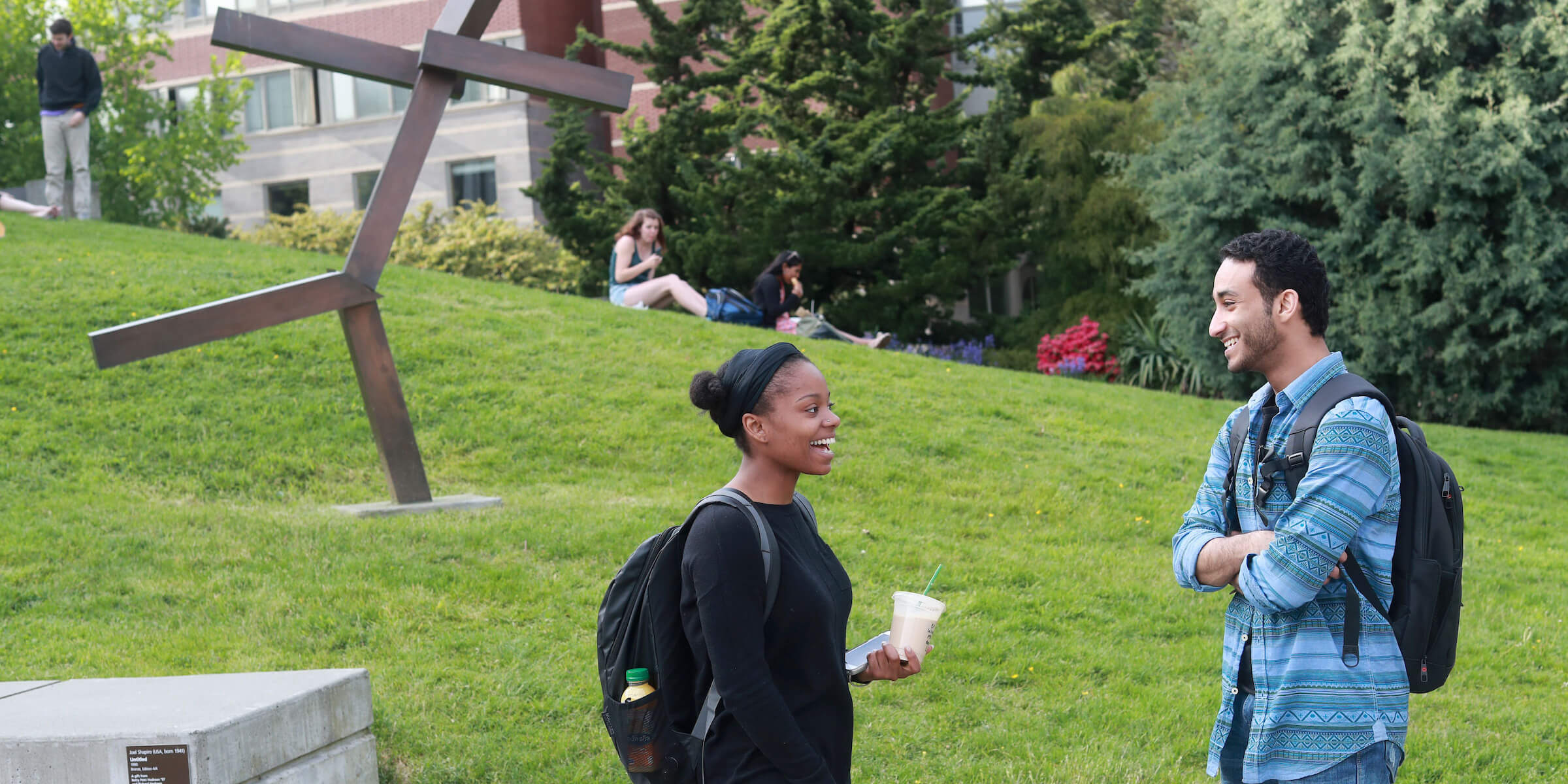 Students sitting in the sun on the lawn in front of the Library