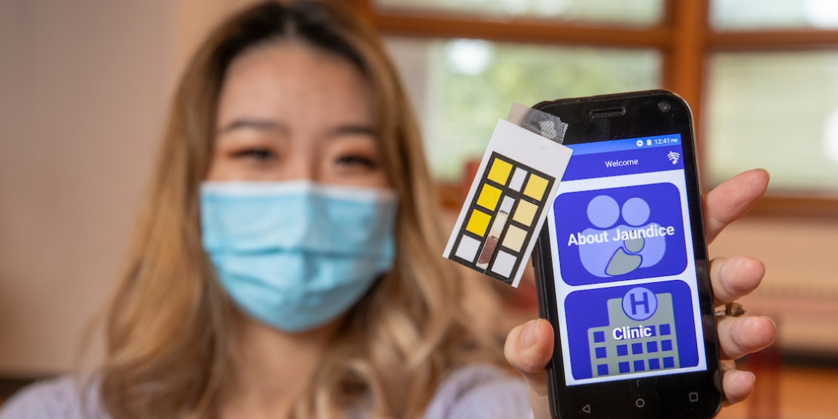 Student holds up smartphone with app and test strip on screen.