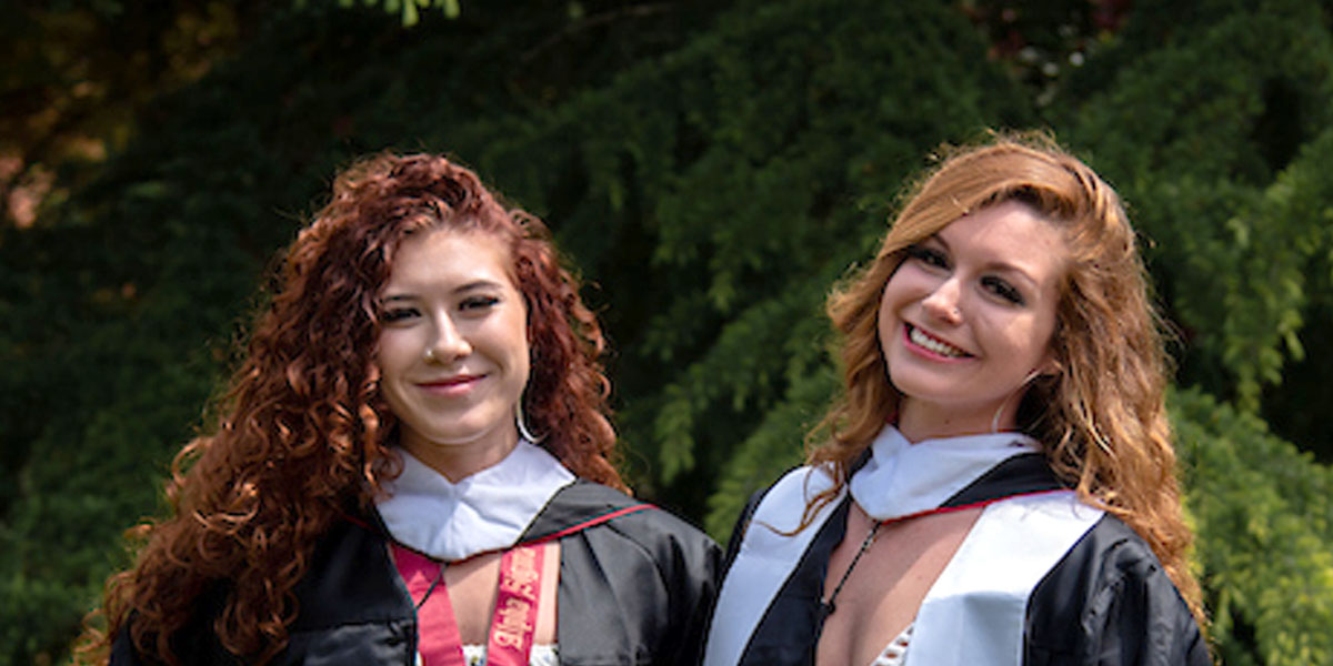 Amber Rodriguez-Munoz and Eva Rodriguez posing on campus in their graduation gowns.