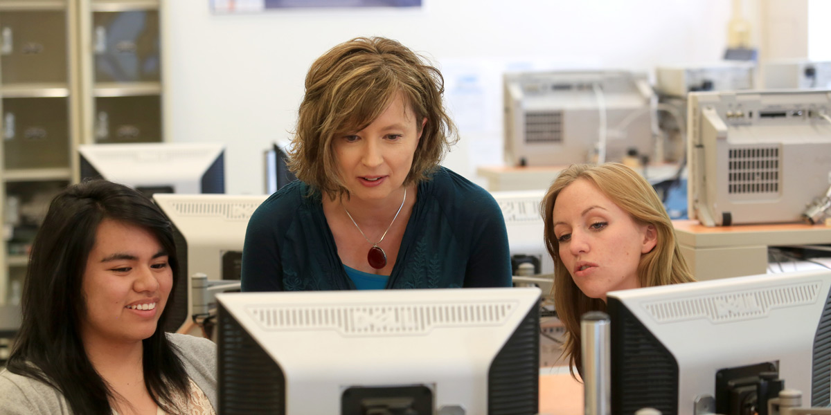 Agnieszka Miguel helping two students on a computer