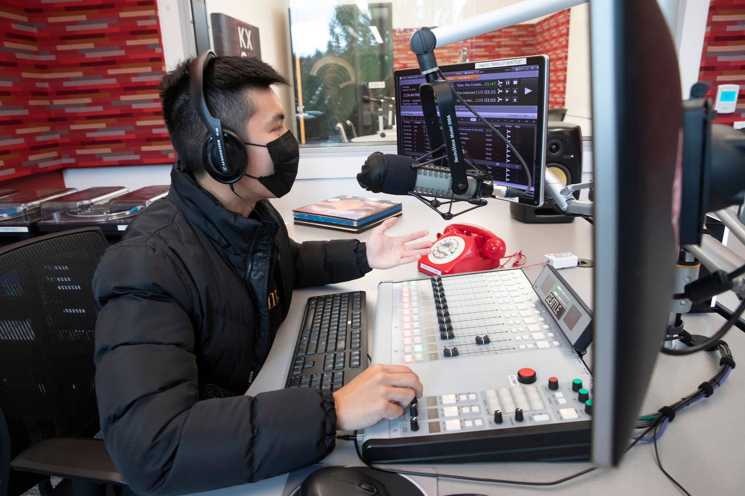   student sitting in front of a microphone and sound engineering station at KXSU