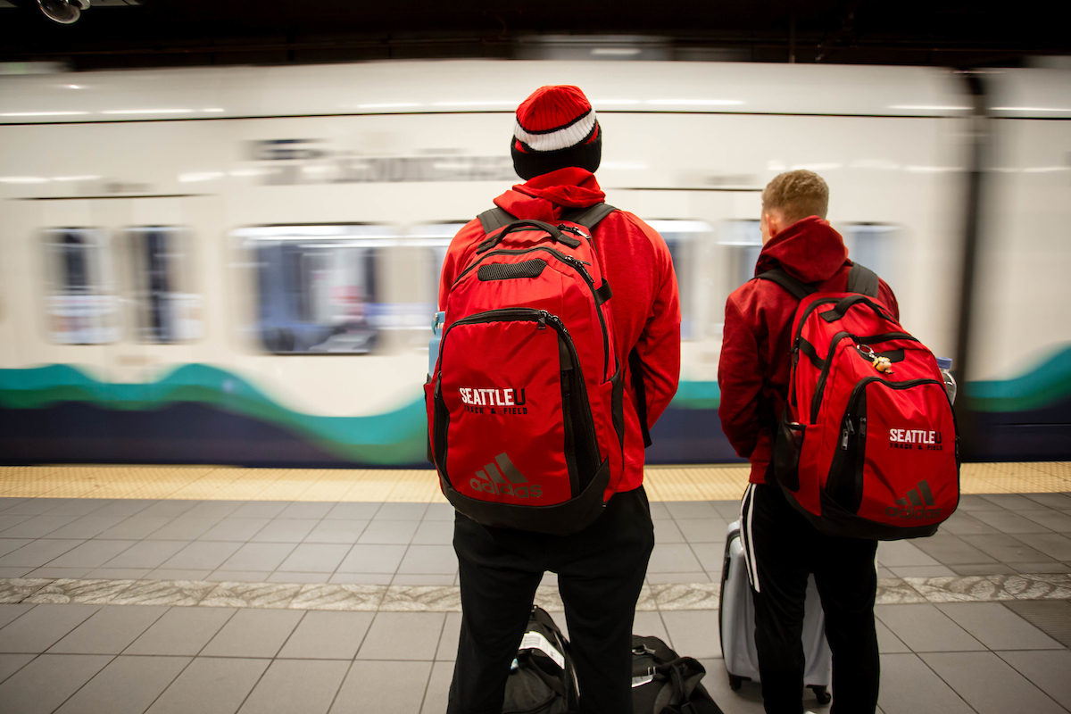 two students stand and chat on the station platform as a train arrives